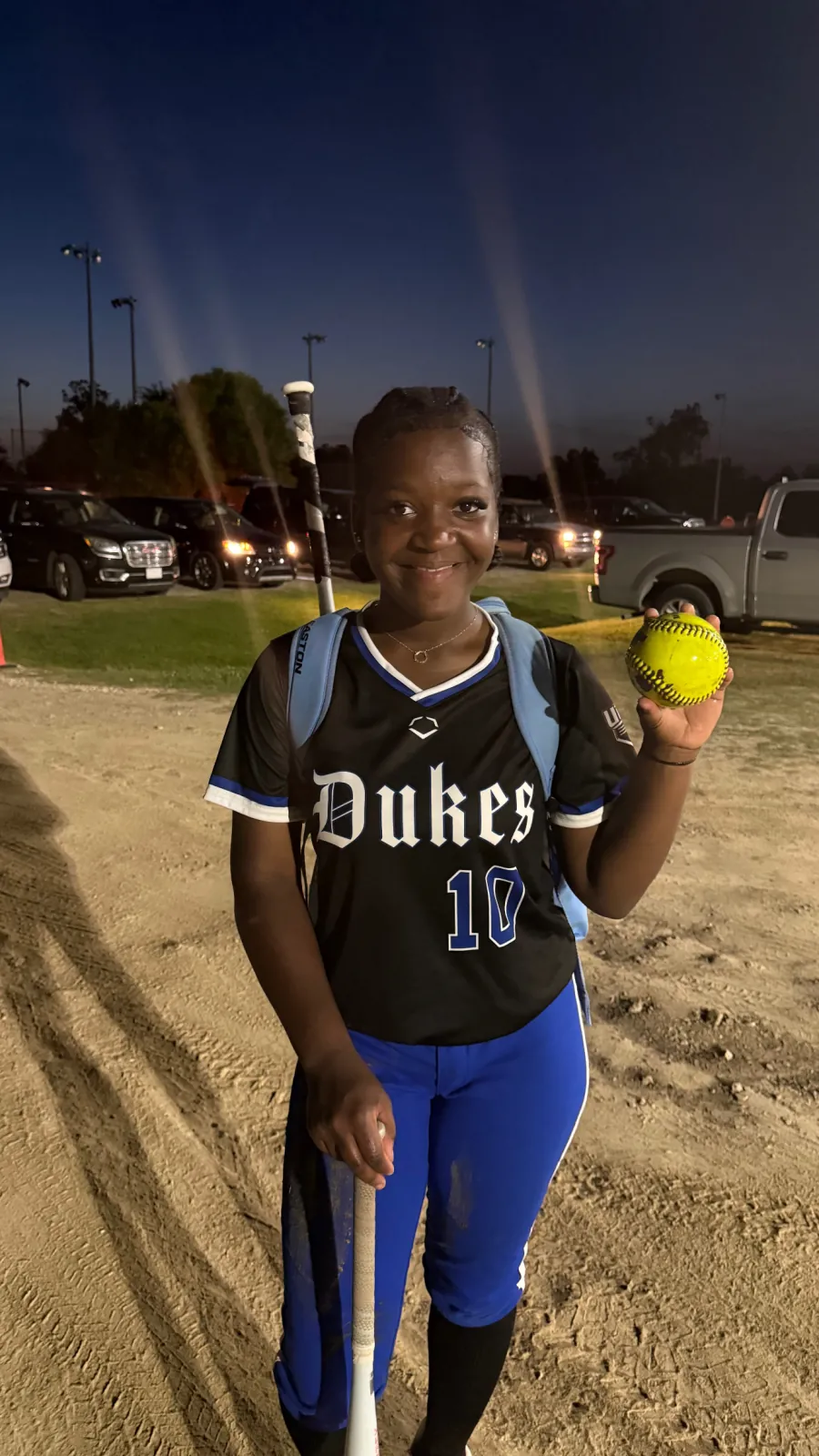 Kennedi Fair (#10) smiling in her Louisiana Lady Dukes uniform, softball and bat in hand at dusk