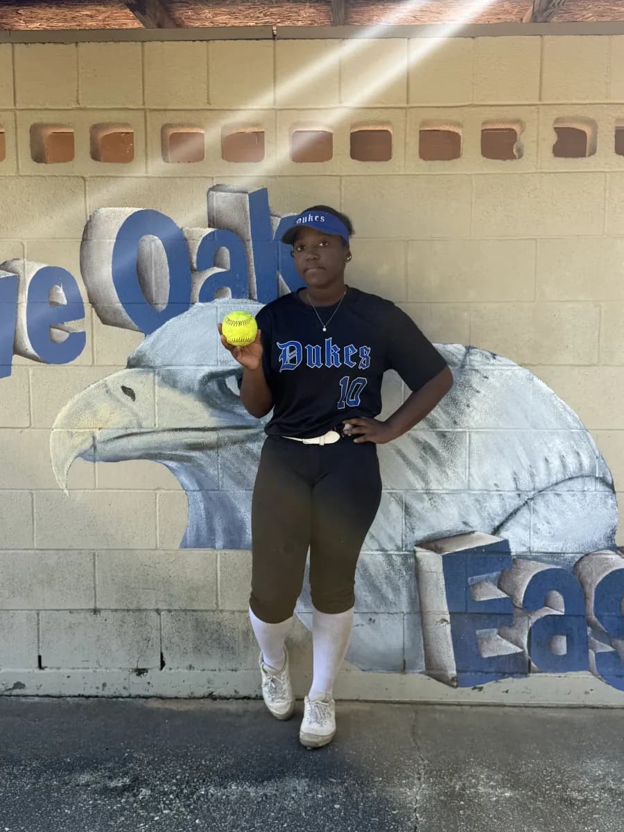 Kennedi Fair (#10) in her Louisiana Lady Dukes uniform holding a softball in front of an eagle mural